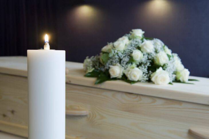 A burning candle with a coffin and a flower arrangement on the background in a mortuary generic funeral photo: candle, coffin and flowers